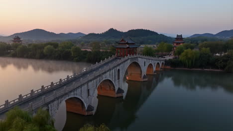 traditional chinese stone bridge and pavilions over a calm lake at dawn