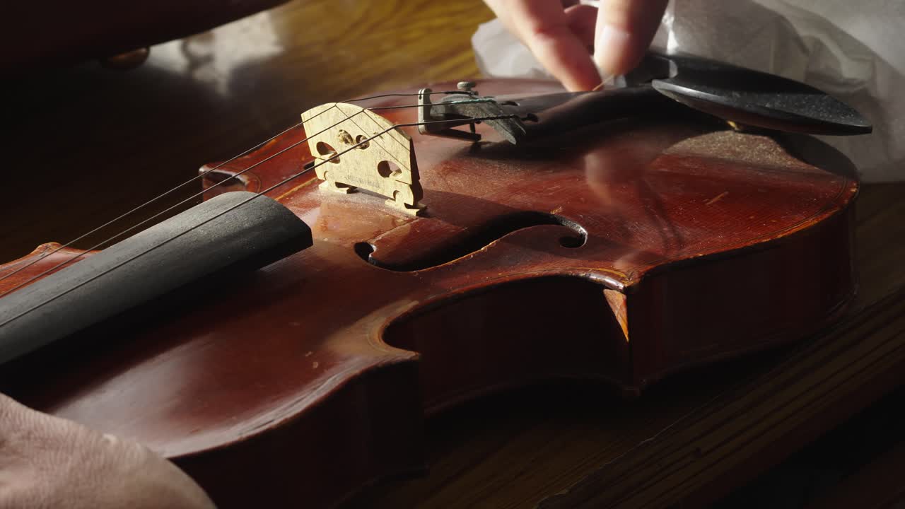 Close-up of musician cleaning antique violin wooden body casing
