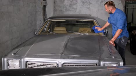 man cleaning a vintage car's windshield in a garage