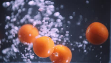 Tomates-Cherry-Cayendo-En-Cámara-Lenta,-Frutas-Flotando-En-El-Agua-Sobre-Fondo-Negro