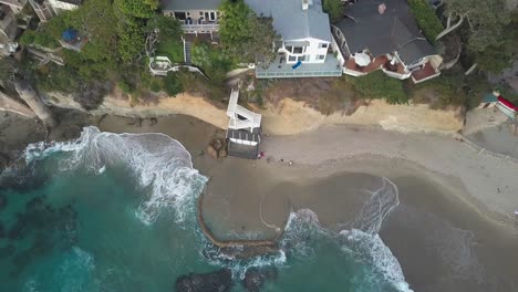 Aerial,-drone-shot-panning-the-shore-of-Victoria-beach-and-houses,-Pirate-Tower,-waves-crashing,-in-Laguna-Beach,-California,-USA