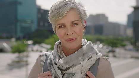 close-up-portrait-of-mature-caucasian-business-woman-smiling-cheerful-at-camera-enjoying-listening-to-music-using-earphones-in-sunny-urban-city