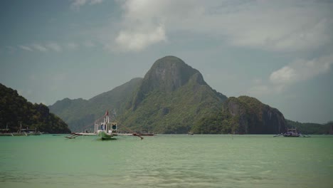 El-Nido,-Philippines---Boats-Floating-By-The-Sea-During-Sunny-Day-With-Green-Mountain-In-The-Background---Wide-Shot