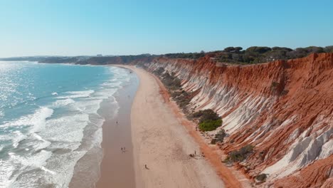 tourists and locals walking along beautiful golden sand on praia da falesia, aerial trucking pan