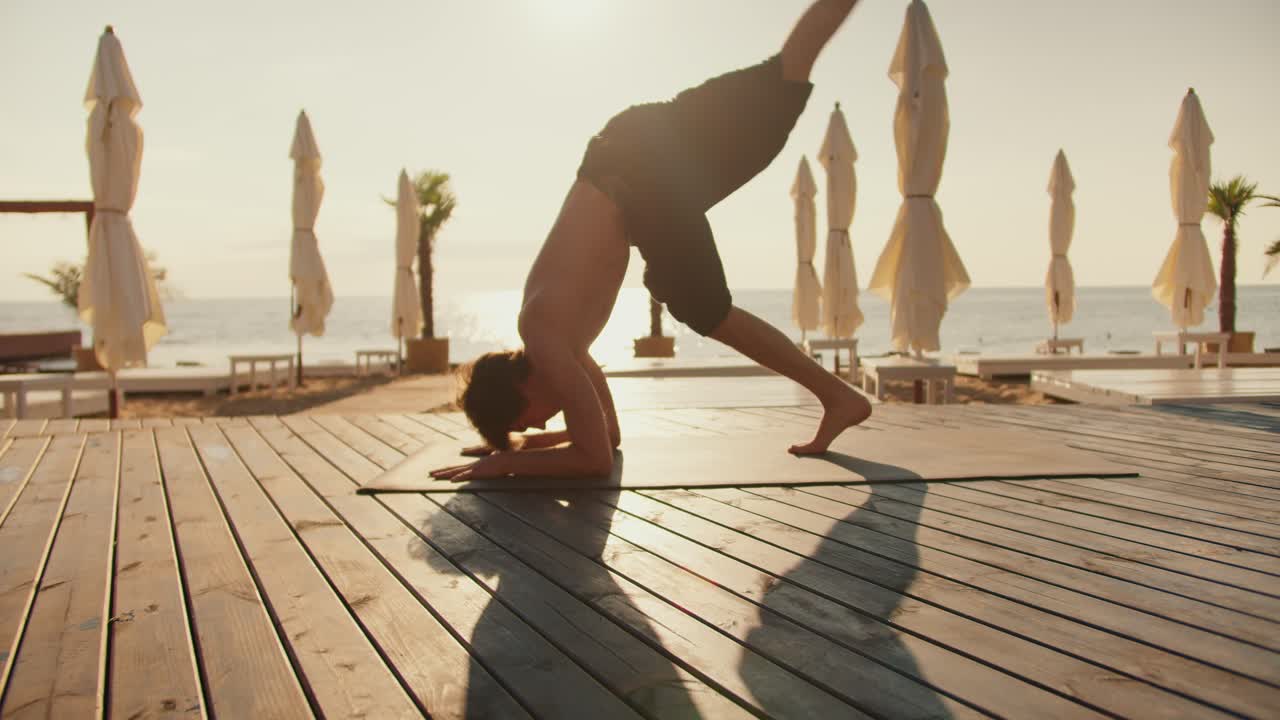 The guy stands on his head on a special mat on a sunny beach. Yoga classes