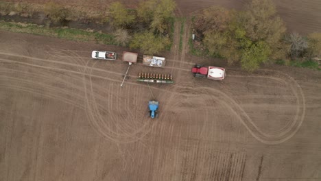 aerial look down view of commercial farming as seeds are loaded into planting machine towed behind tractor