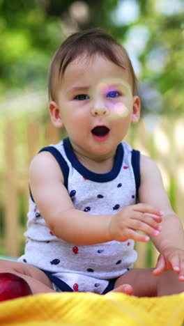 cute baby sitting in the summer garden looks at soap bubbles flying by. toddler sits still and then wants to reach the camera. blurred backdrop. vertical video