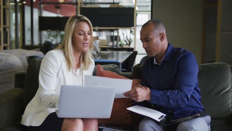 two diverse business colleagues using laptop and discussing paperwork in a casual meeting