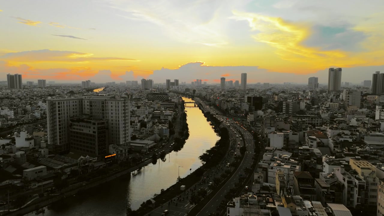 Altın gün batımında Ho Chi Minh Şehri'nin sinematik havadan uçuşu. Yoğun Saygon silüeti üzerinde canlı turuncu bulutları yansıtan şehir nehrini içerir. Seyahat veya şehir b-roll'u için mükemmel.