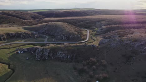 Dobrogea-gorges-during-sunset-with-winding-road-through-hilly-terrain,-aerial-view