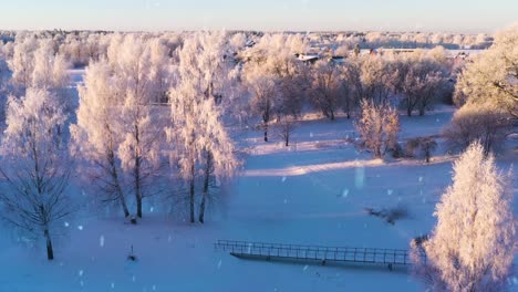 Ascend-over-frozen-lake-to-reveal-township-while-snowing,-aerial-view