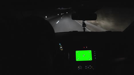 man driving modern sports car on a highway in evening time using navigation on his smart phone with blank green screen