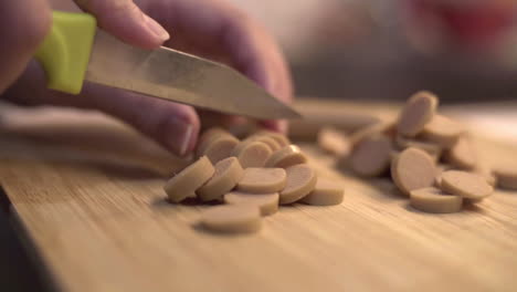 Close-up-of-Caucasian-hands-cuts-small-sausages-with-knife-on-wood-board