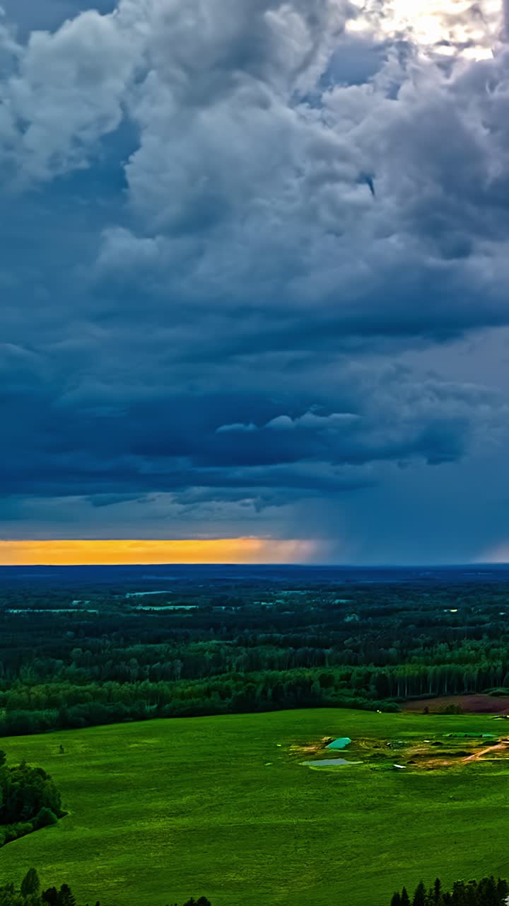Timelapse aereo verticale cattura nuvole temporalesche drammatiche che sfrecciano su un lussureggiante prato e foresta lettone con una vivida luce dorata dell'alba che splende lungo l'orizzonte.