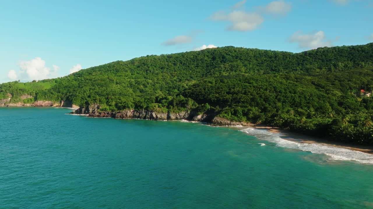 Drone panning left over lush Guadeloupe coastline and turquoise sea