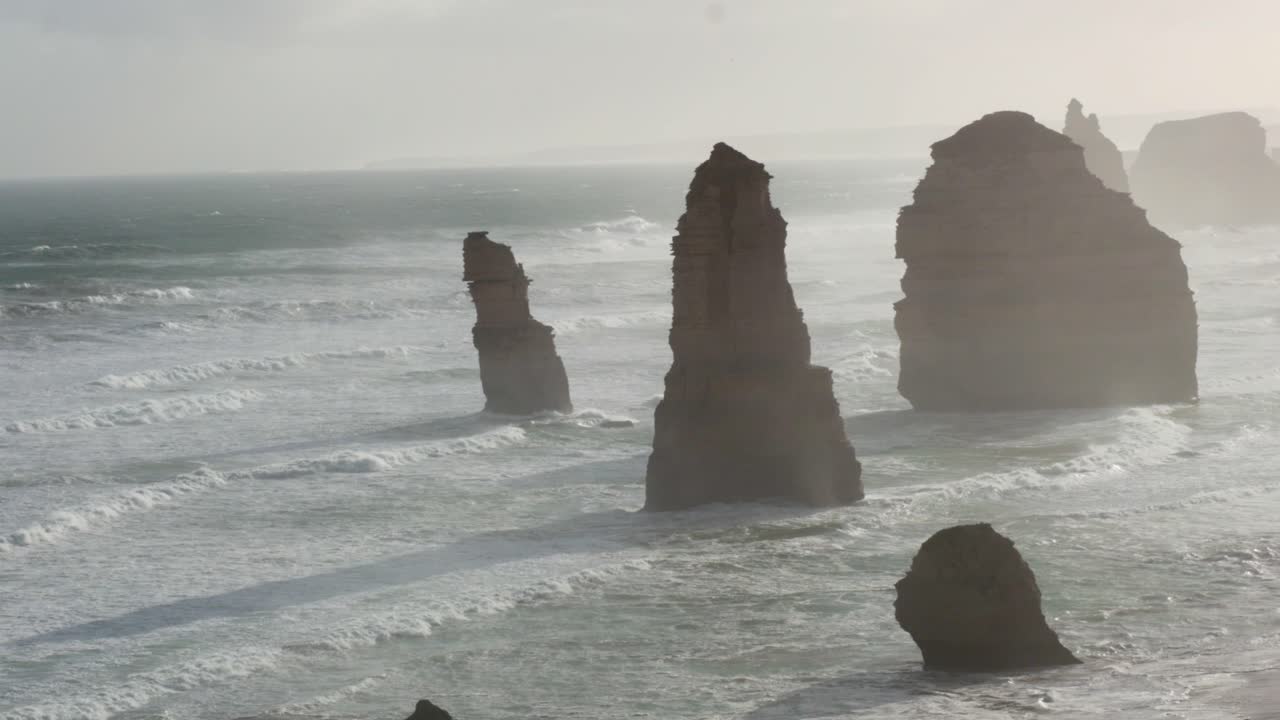 Iconic limestone stacks along Australia's coast, captured at sunrise with soft lighting and gentle waves creating a serene atmosphere