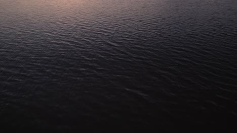 Slow-drone-tilt-up-with-fast-forward-movement-flying-in-from-the-sea-over-the-beach-in-Dundalk-Bay-while-the-sun-sets