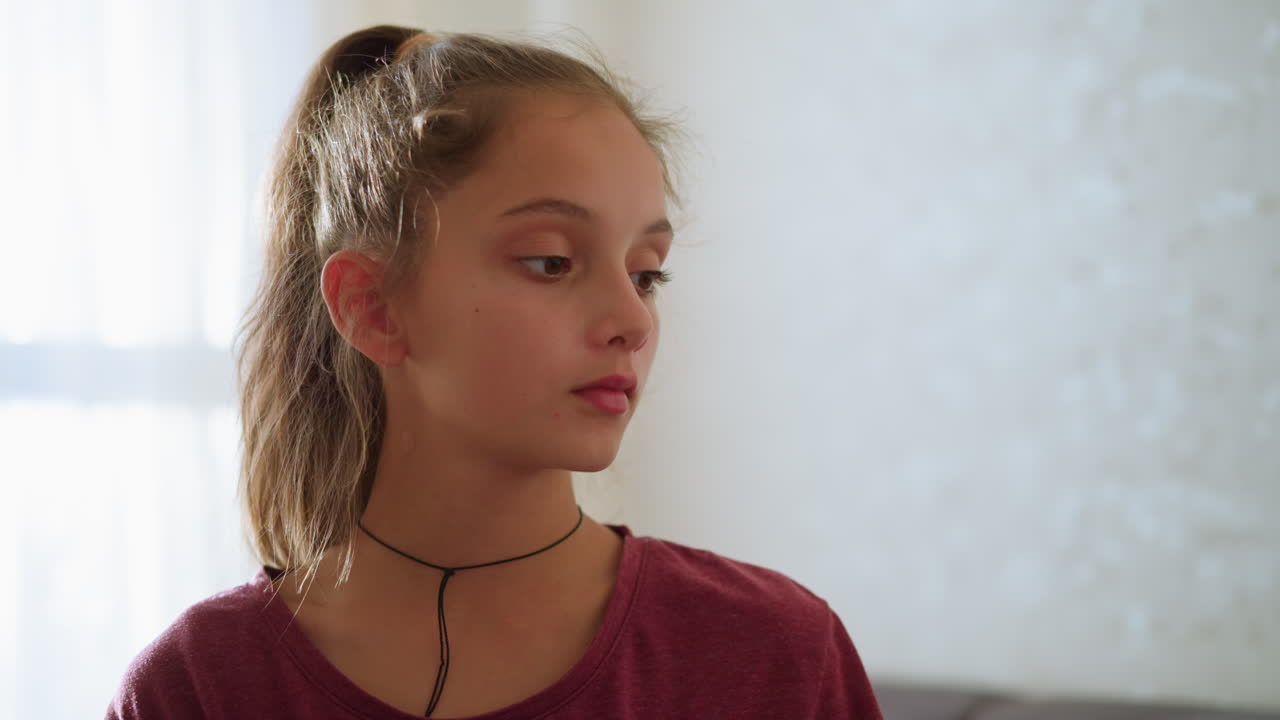 Cute girl looking thoughtfully at someone in the background, soft light illuminating her face, indoor setting with gentle atmosphere, concerned or curious expression, calm moment