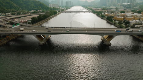 Aerial-tilt-shot-cars-driving-on-highway-over-a-wide-waterway-bridge,-HongKong