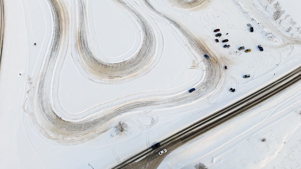 Aerial view rising around cars driving on a rural ice racing track, winter day