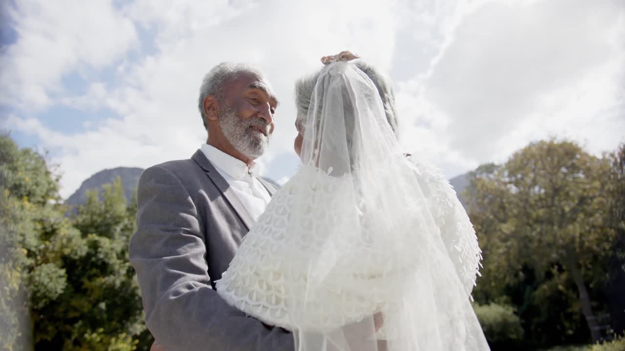 Glade ældre multietniske par går og danser til bryllup i haven, slow motion