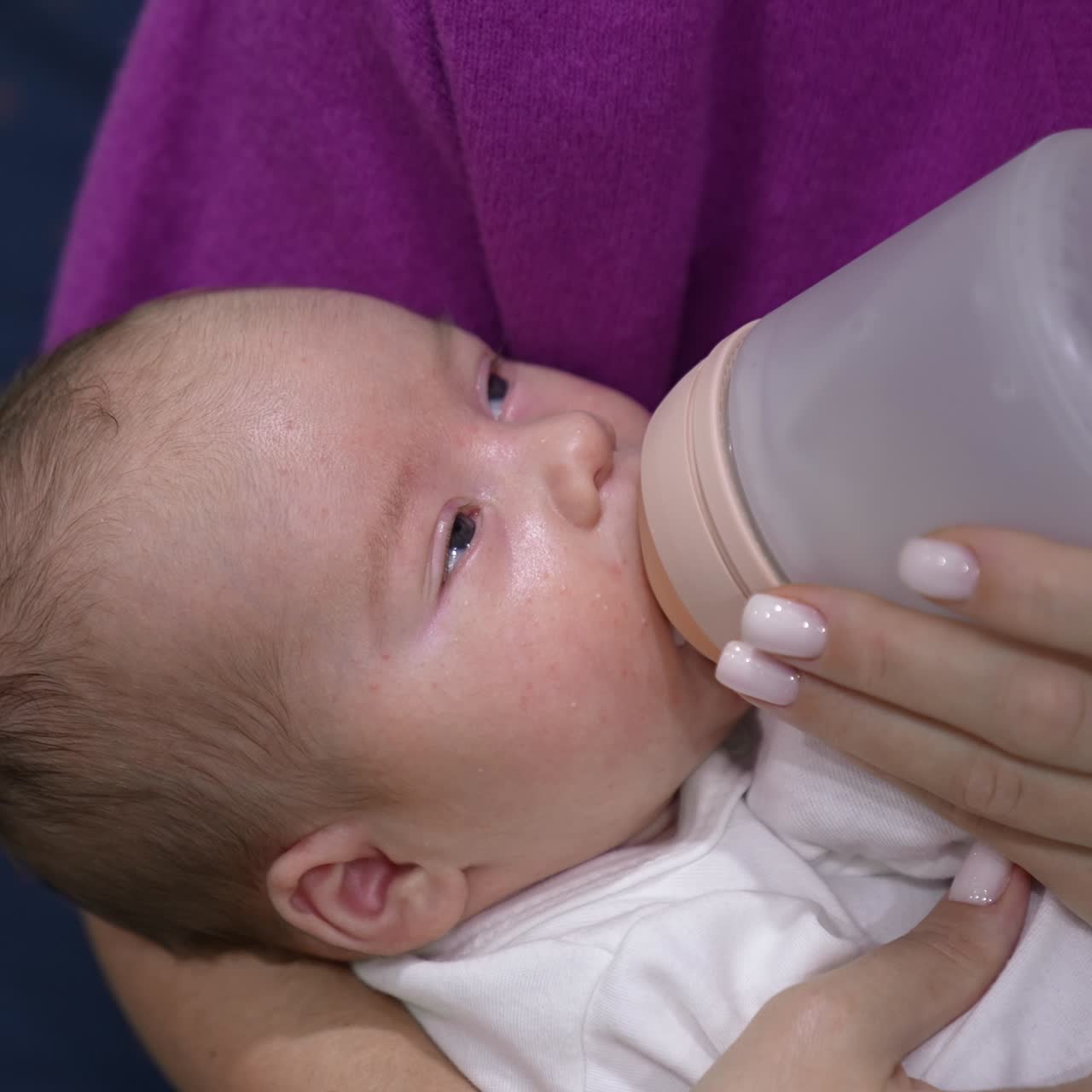 Sleepy baby finishing his milk in the bottle. Little child in mother's arms falling asleep gradually while having meal. Close up