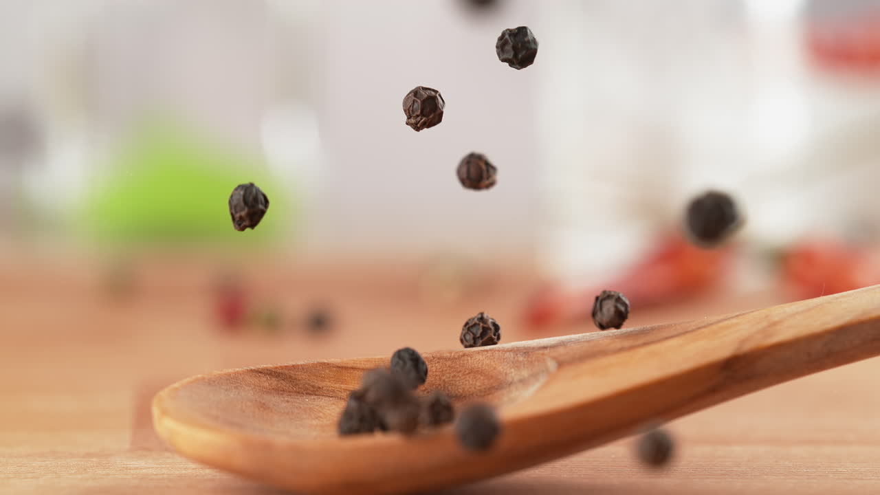 Spoon Of Black Pepper Falls Onto The Kitchen Countertop, And The Spice Scatters in Macro and Slow Motion