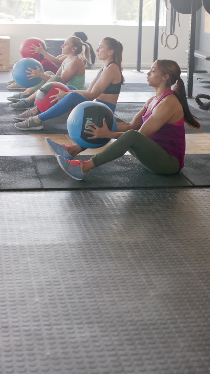 Vertical video of diverse sportswomen exercising with medicine balls at gym in slow motion