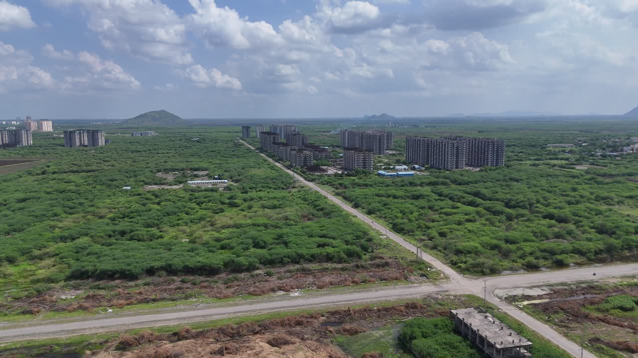Overhead view of a road cutting through the countryside, surrounded by lush fields with buildings in the background.
