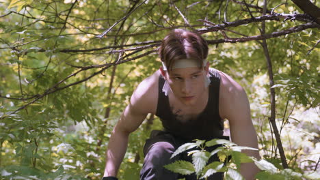 soldier walking and bending under low hanging branches in lonely forest, navigating undergrowth with cautious posture as sunlight filters through leaves creating dappled shadows on green canopy