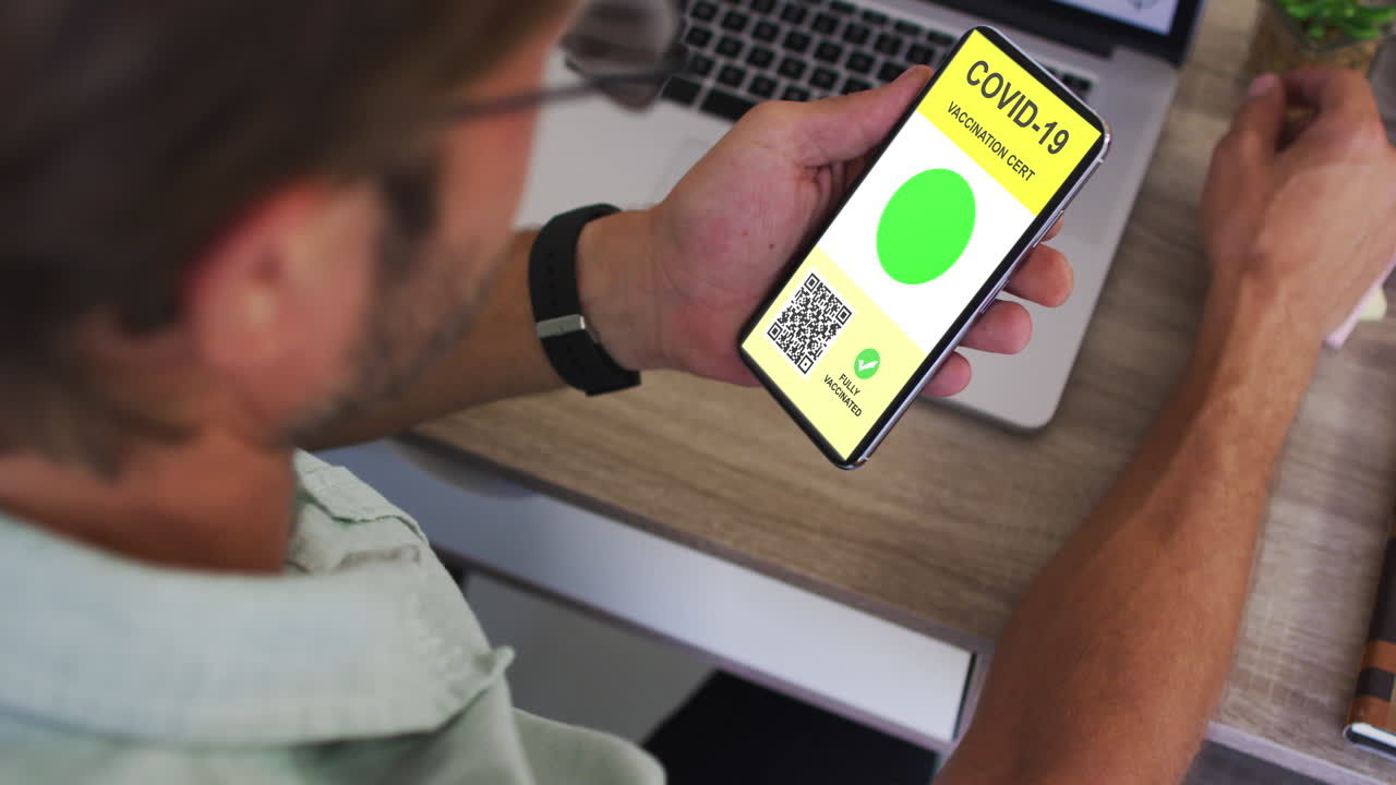 hombre en el escritorio sosteniendo un teléfono inteligente con certificado de vacunación contra la covid y código qr en la pantalla