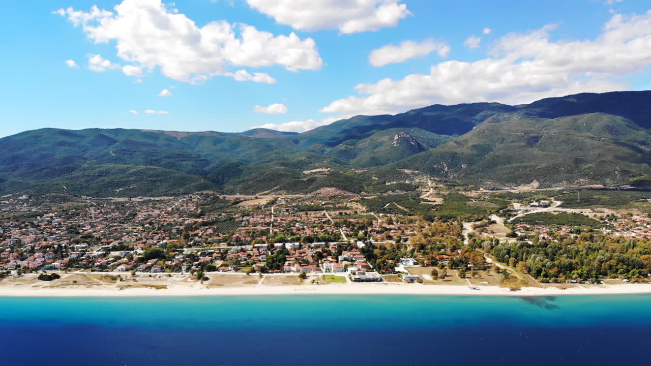 Panorama of the Asprovalta located on the Aegean sea coast with buildings and greenery, green hills. Long beach along the town. Sunny day, view from the drone. Greece