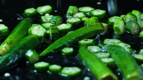 slow motion shot of chopped green chili pieces and entire chilis splashed with rain or tap water on a black surface