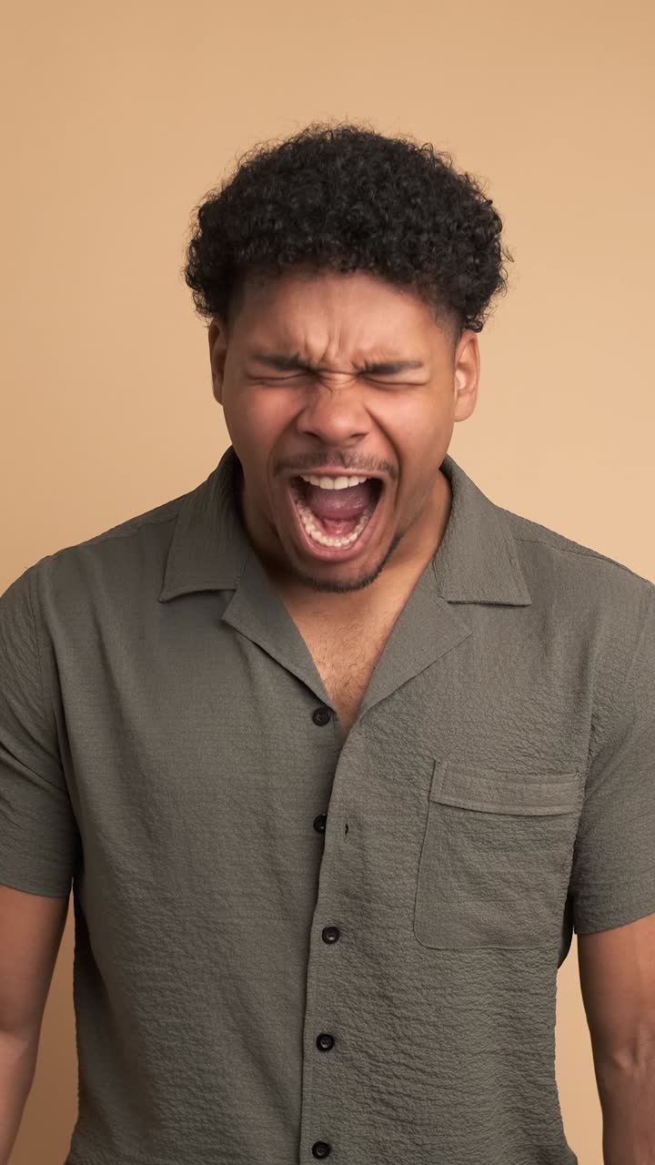 Frustrated young man screaming in beige studio