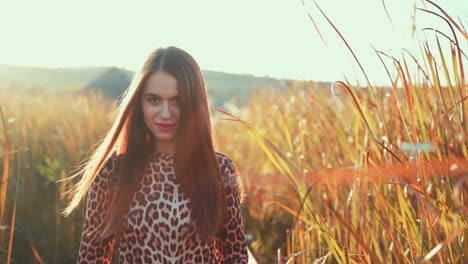 young beautiful caucasian brunette woman smiling and walking in tall green grass field towards camera on bright sunny day, close up portrait pull back