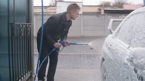 young man in leather jacket applying foam on silver sportcar with special jet on self-service carwash