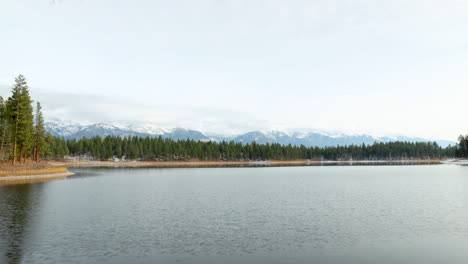 Lapso-De-Tiempo-De-Un-Lago-Suave-Y-Vacío-Con-Montañas-Cubiertas-De-Nieve-En-El-Fondo-En-Un-Hermoso-Día-Soleado,-Toma-Amplia-Con-Espacio-Negativo