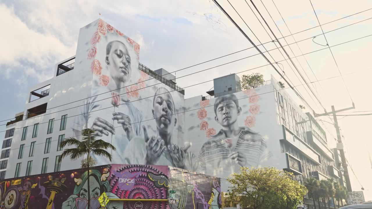 Low-angle view of a mural at Wynwood Art District, Miami, depicting African and Latin children holding roses, with one extending hands in a prayer-like gesture.