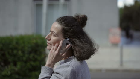 mujer madura atractiva caminando por la calle de la ciudad con un teléfono inteligente.