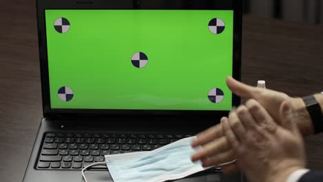 la mano del hombre toma desinfectante y lo usa cerca de la computadora portátil con pantalla verde. coronavirus