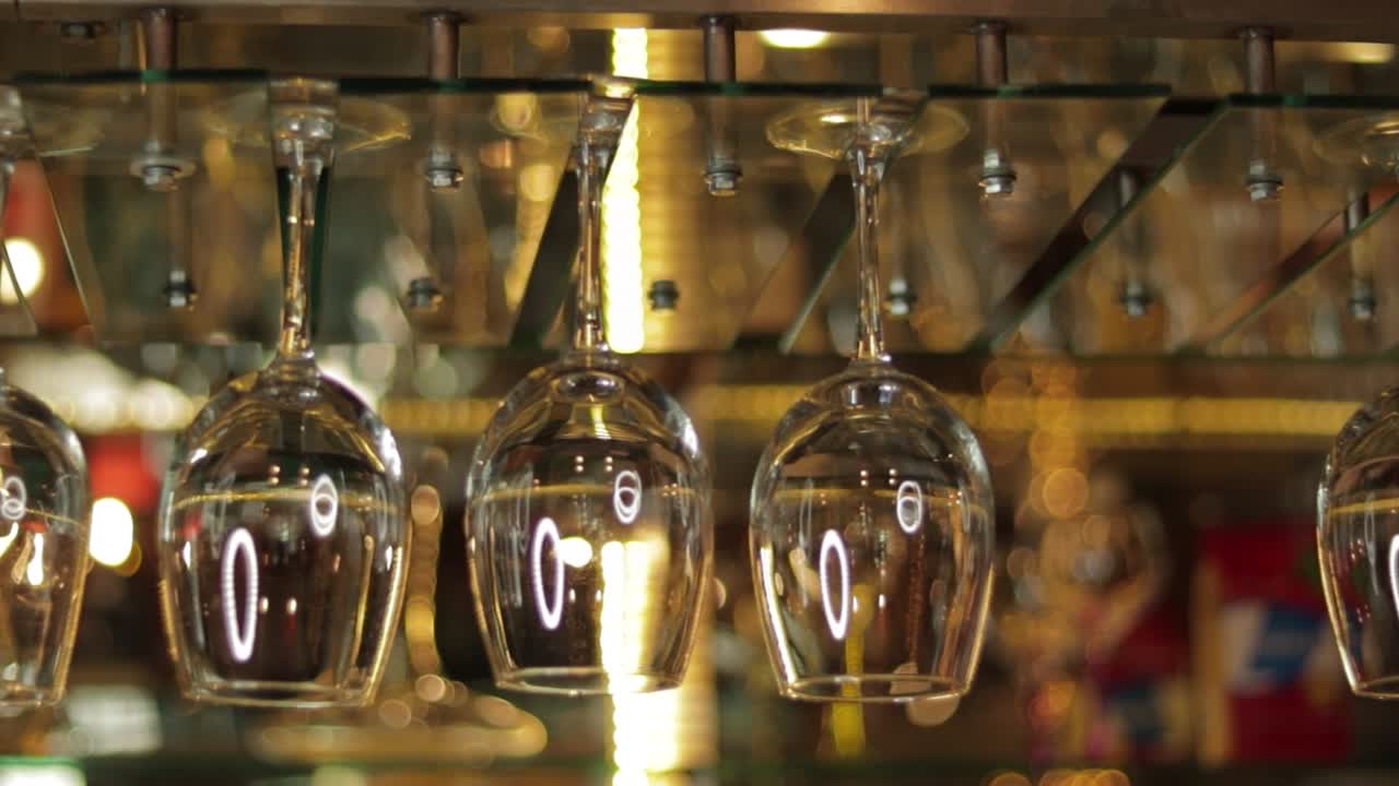 Empty wine glasses hanging upside down from overbar glass rack in bar