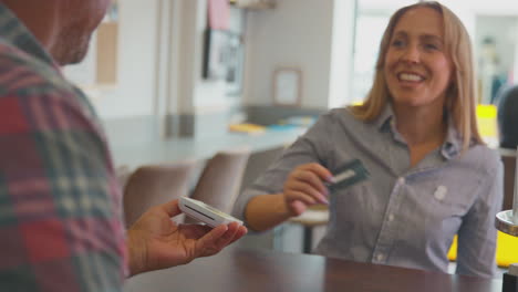 female customer making contactless payment for takeaway drink in coffee shop using mobile phone