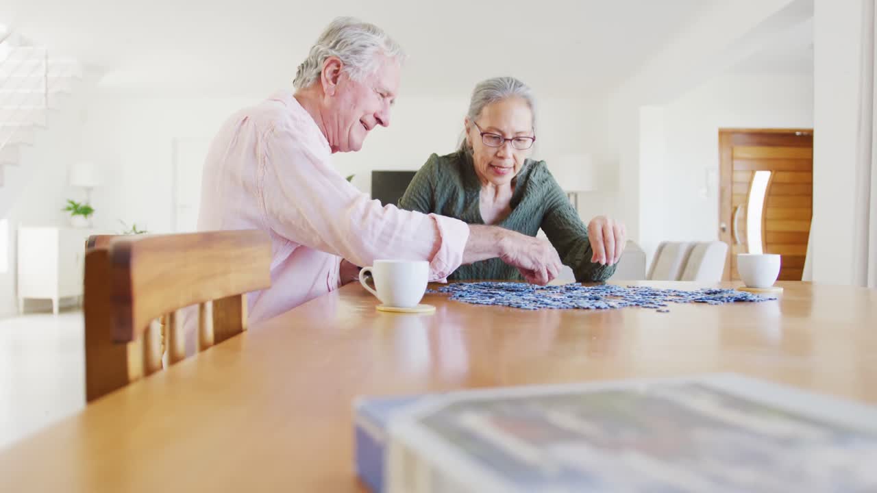 feliz pareja de ancianos diversos sentados a la mesa y haciendo rompecabezas