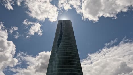 sun in blue sky hides behind tall glass skyscraper as clouds roll in