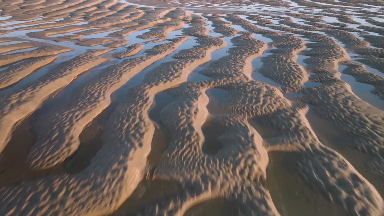 Tidal sand ripples with seawater pools at golden hour. Fast flight over.