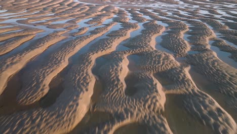 tidal sand ripples with seawater pools at golden hour. fast flight over.