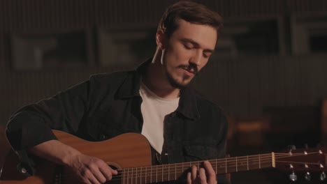 a handsome guy plays an acoustic guitar in an abandoned cinema. the musician sings a song and accompanies on the guitar