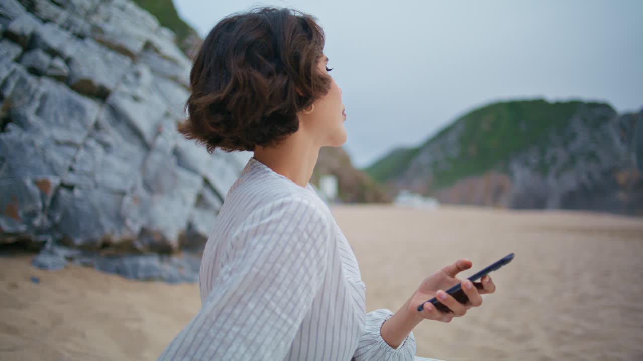 Primo piano di una donna che tiene lo smartphone in spiaggia nel fine settimana. Donna elegante che si riposa in riva al mare.