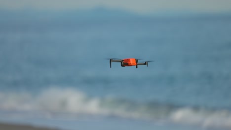 orange little drone flying over the shore of a beach