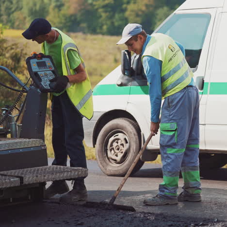 workers make road asphalting on the natural background of trees. male workers in protective uniform are working on one side of the road. new asphalt on the highway.